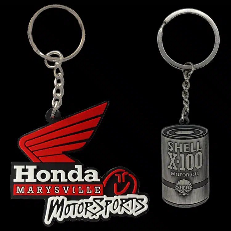 Two custom key chains made two different ways: a red Honda Marysville Motorsports wing in PVC and a pewter Shell X-100 oil can fob