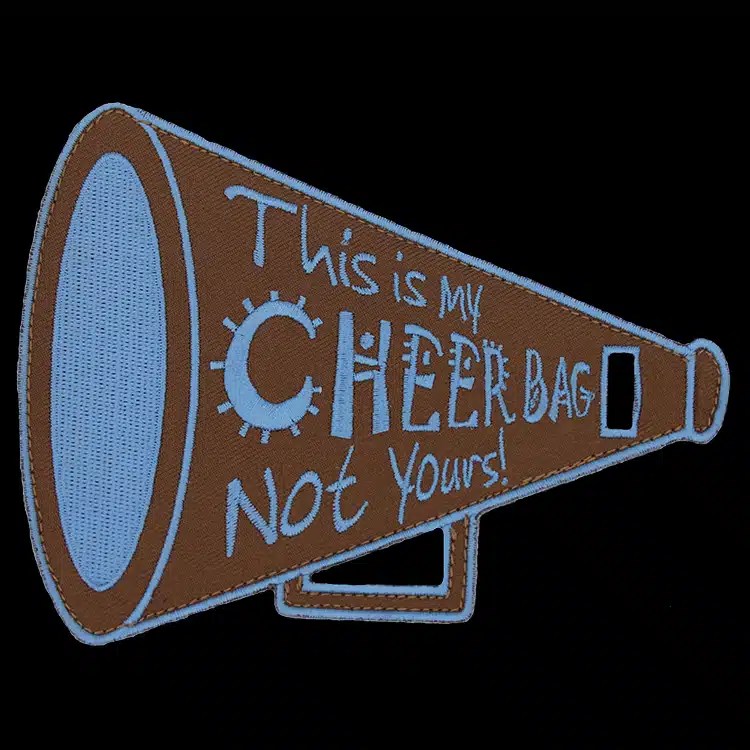 Embroidered luggage tag cut in the shape of a megaphone, reading This is my Cheer Bag Not Yours in light blue thread on brown, with a strap slot.