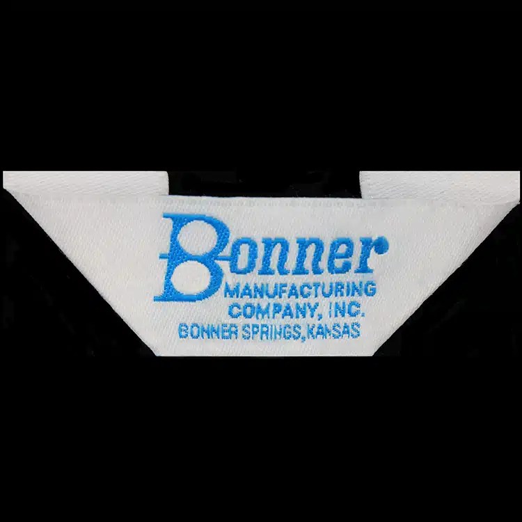 White woven garment label folded at both ends, with a blue script logotype and small blue lettering beneath.
